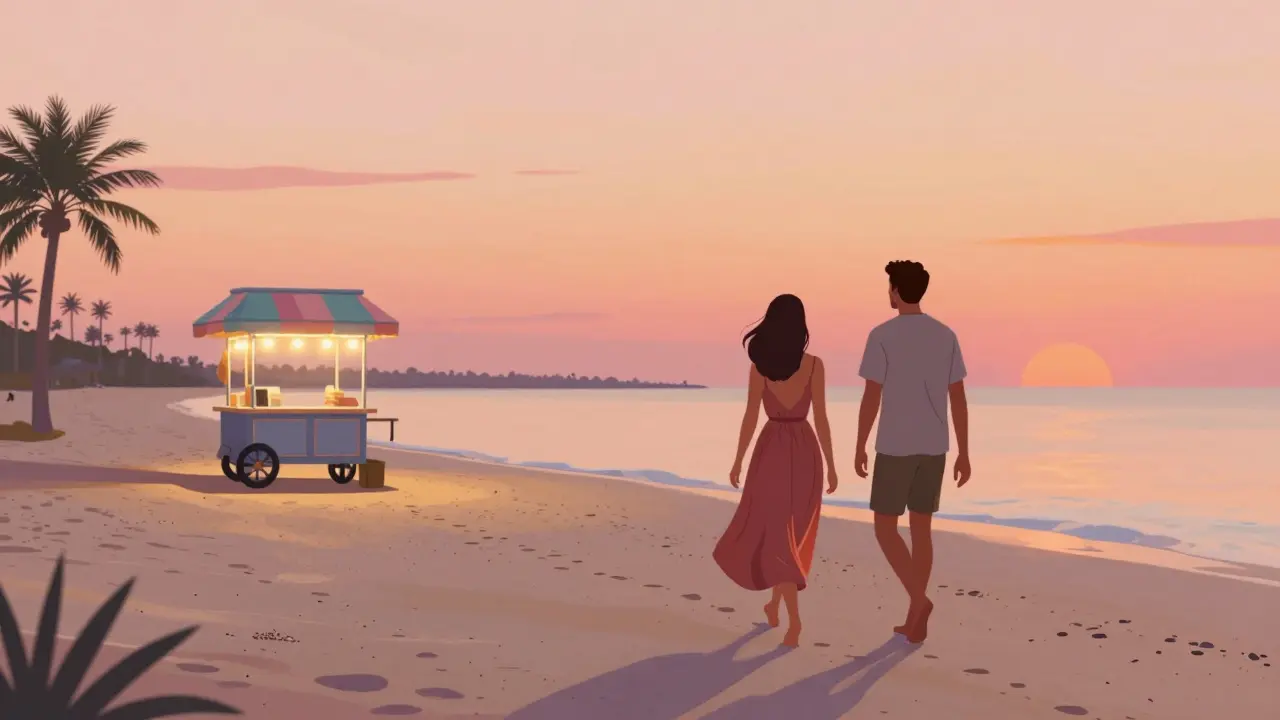 Two people walking barefoot along La Mer Beach at sunset, ice cream cart in the distance.