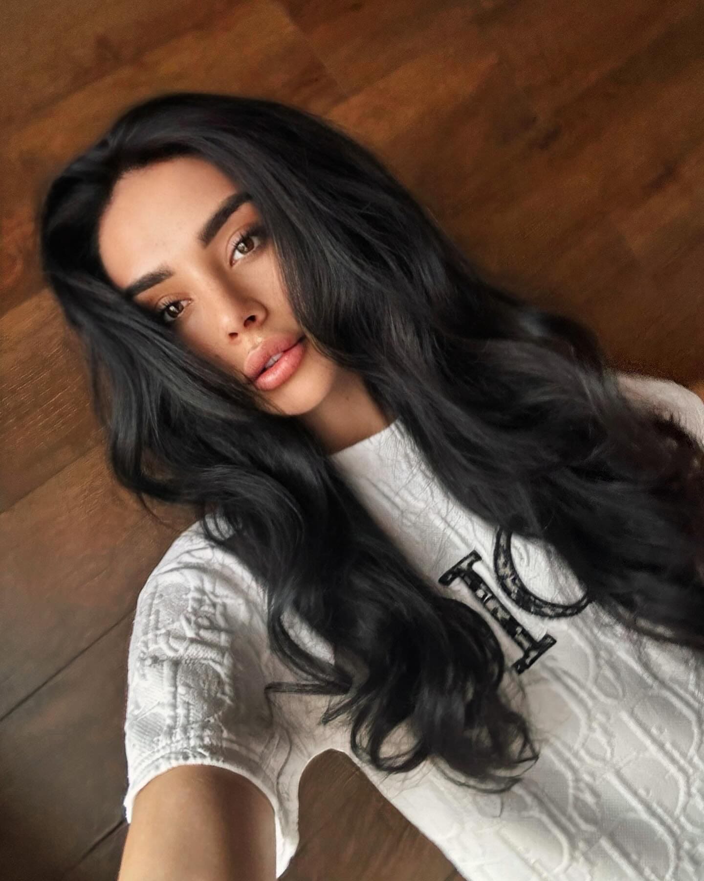 Catherine lies on a wooden floor in a white short-sleeved top with black lettering, looking up at the camera.