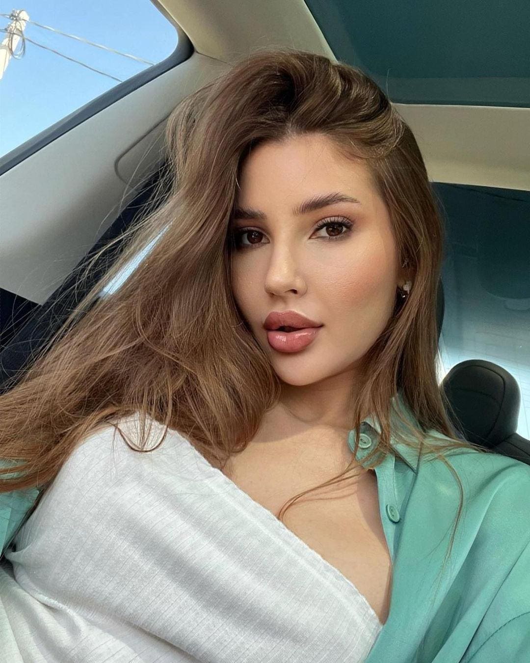 Courtney sits in a car passenger seat, wearing a white top and open mint-green shirt, with a sunroof visible above.