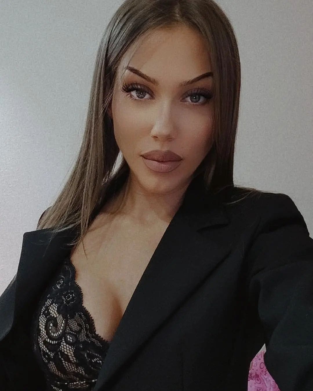 Lucy wears a black blazer over a lace top, posing against a plain light wall.