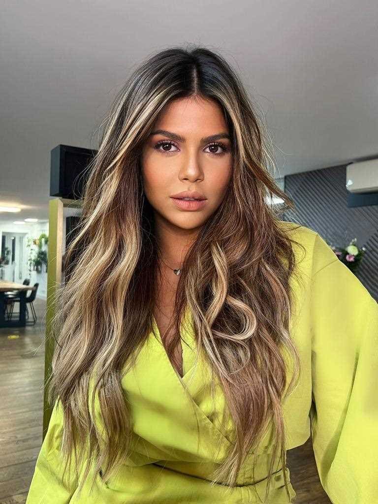 Virginia stands indoors in a lime-green wrap top, facing the camera with a table and chairs behind her.